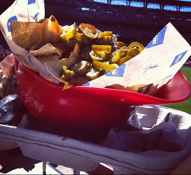 Photo of a fan holding the helmet nachos at a baseball game.
